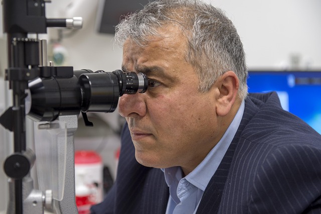 A middle-aged man in a suit jacket leaning forward to look into the eyepiece of a slit lamp device during an eye exam.